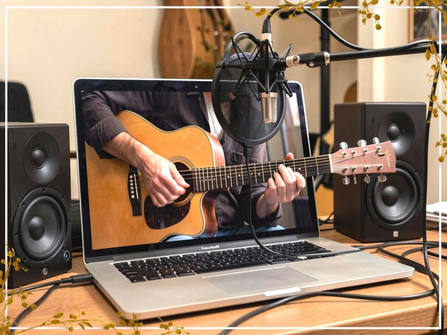 Generated image created by Wombo Dream AI. A conceptual 'out of bounds' digital illustration depicting a laptop computer as an active musician. Stylized arms appear to extend from the device, actively playing an acoustic guitar. A professional microphone hangs suspended over the laptop, positioned to record both the guitar and the audio output (vocals) emerging directly from the laptop's speakers.