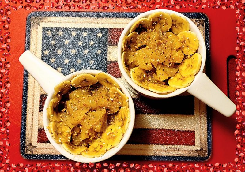 Top-down view of two cozy, white mug-style bowls filled with warm, cinnamon-dusted fried apples and bananas, sitting on a glass cutting board with a red, white, and blue American flag design and decorated with a red jeweled digital frame from Photo Studio Pro app for Android. 
